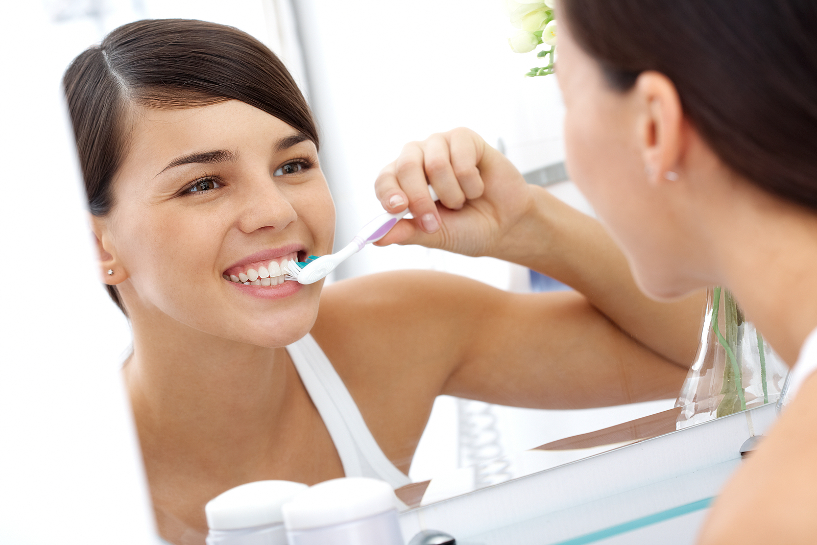 Girl brushes her teeth in the mirror while smiling.