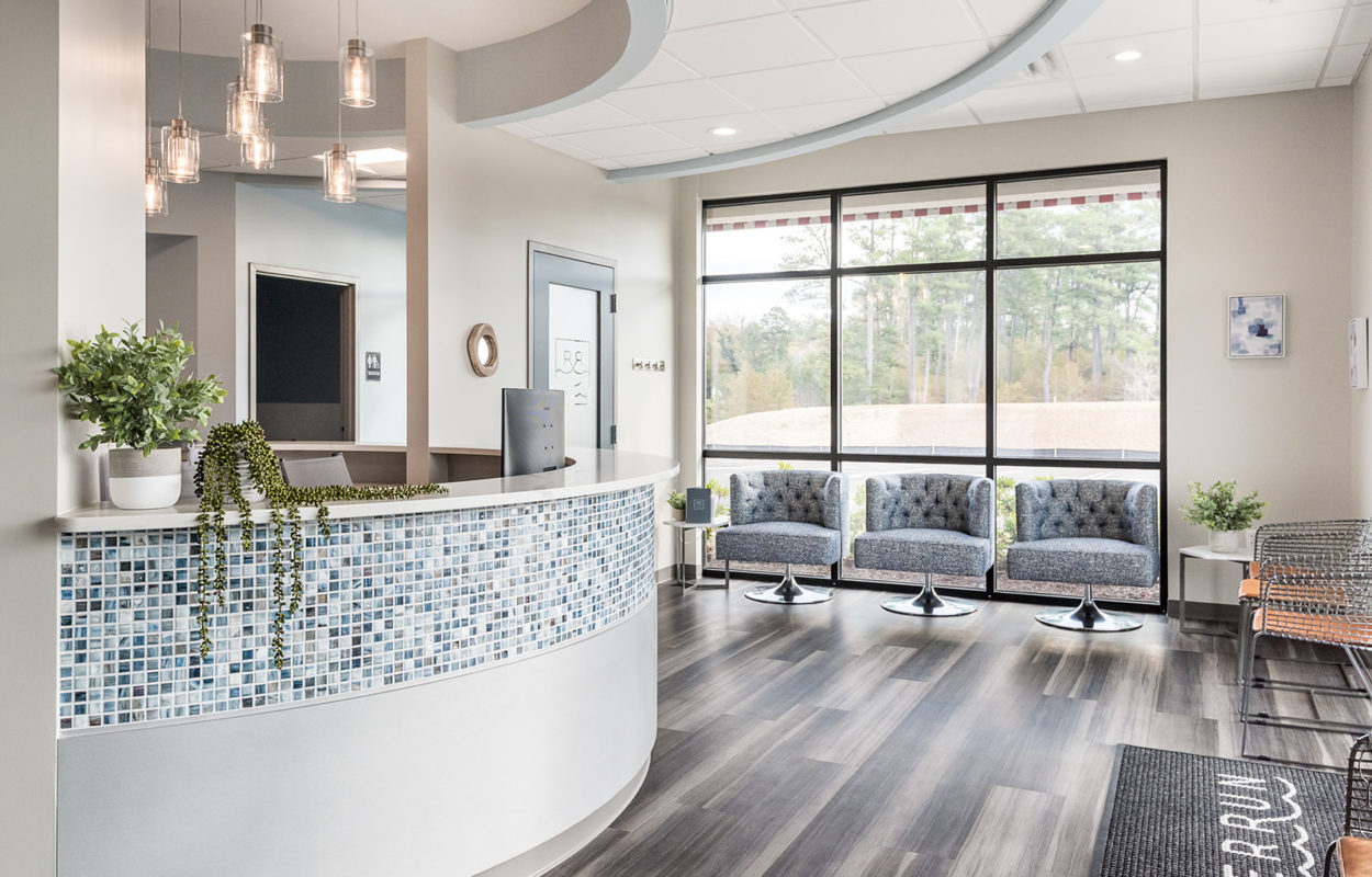 Welcoming dental office reception area with curved front desk and comfortable waiting room seating