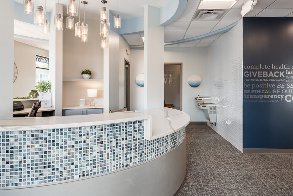 Curved reception desk with mosaic tile accents in a bright and modern dental office lobby