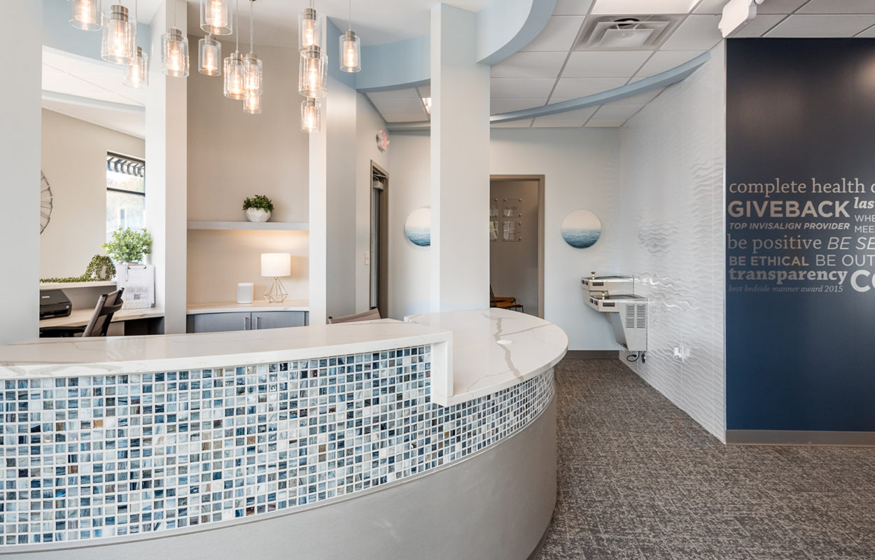Curved reception desk with mosaic tile accents in a bright and modern dental office lobby