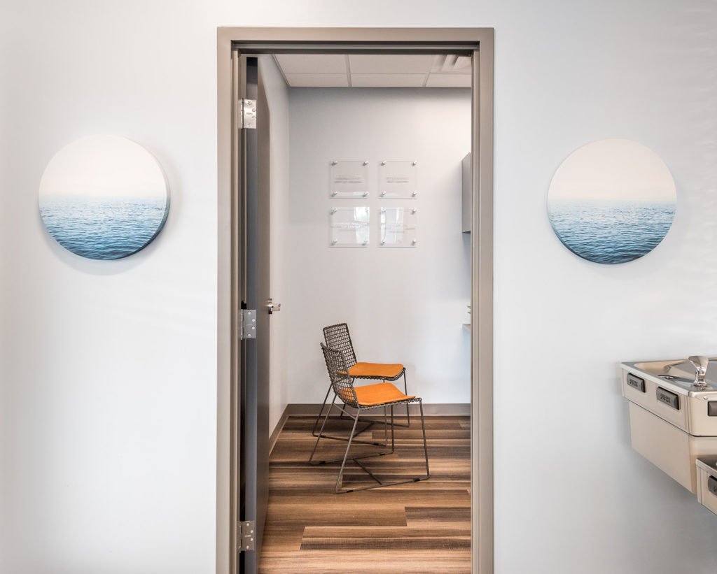 View through a doorway into a modern dental consultation room with seating and decorative wall art