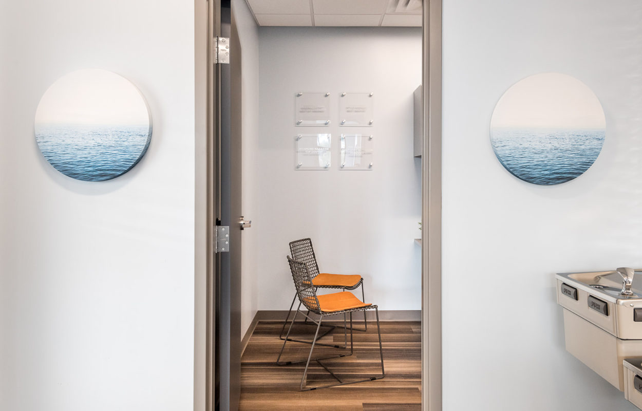 View through a doorway into a modern dental consultation room with seating and decorative wall art