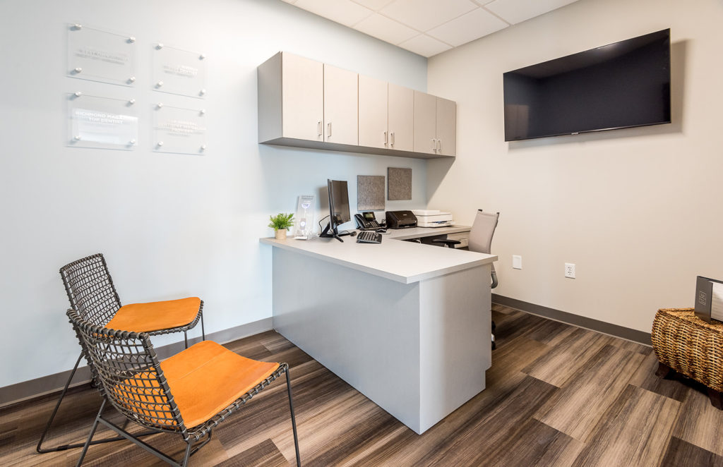 Contemporary dental consultation room with desk, seating area, cabinetry, and wood-look flooring