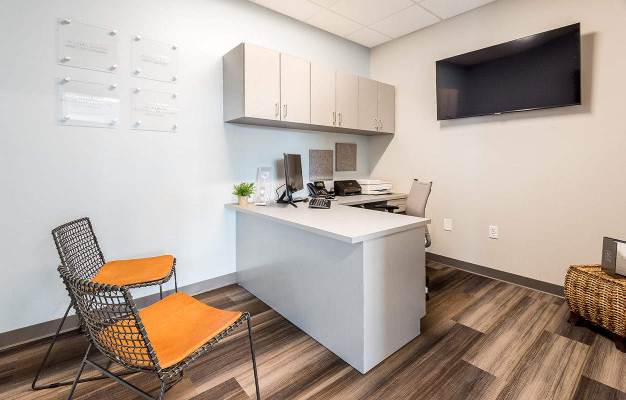 Contemporary dental consultation room with desk, seating area, cabinetry, and wood-look flooring
