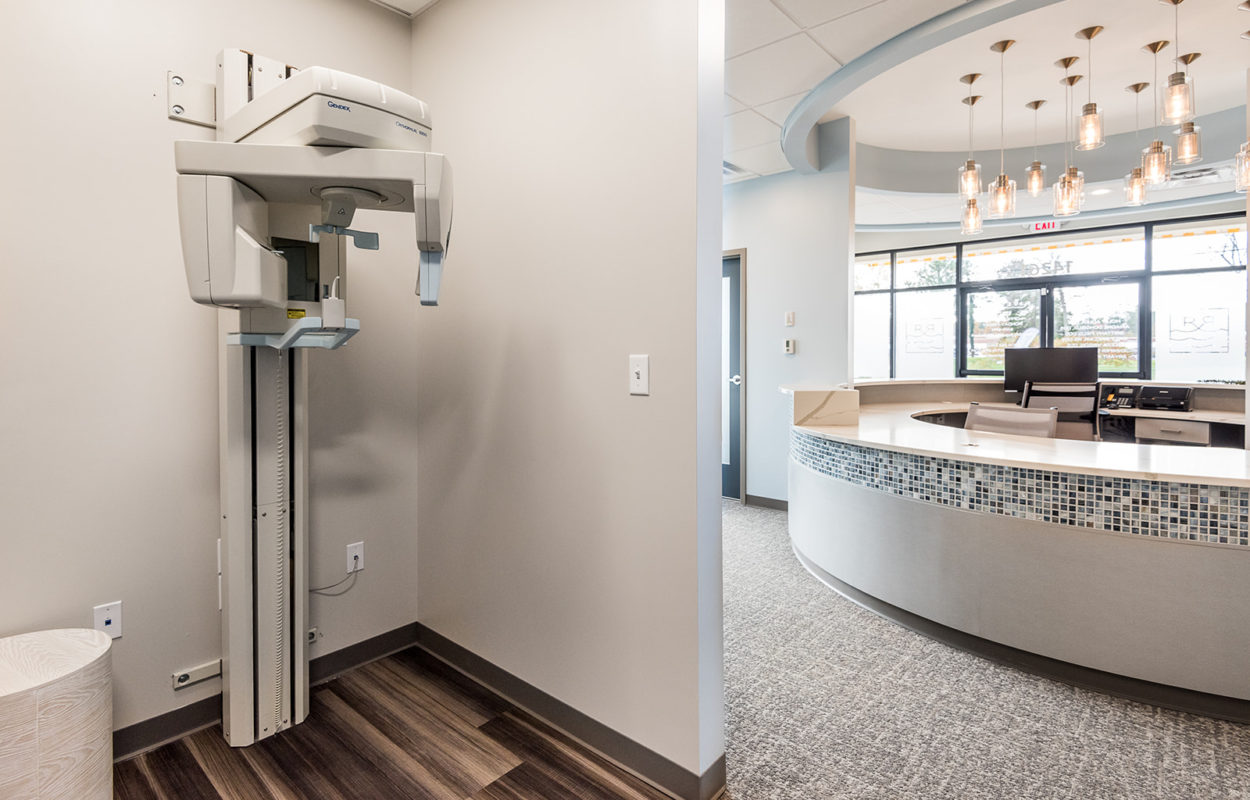 Digital panoramic dental X-ray machine positioned in a clean, modern dental office hallway