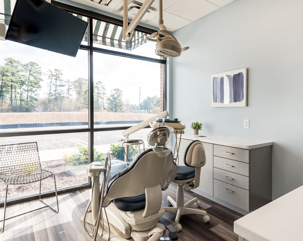 Bright dental operatory featuring a treatment chair, workstation, and floor-to-ceiling windows overlooking the exterior