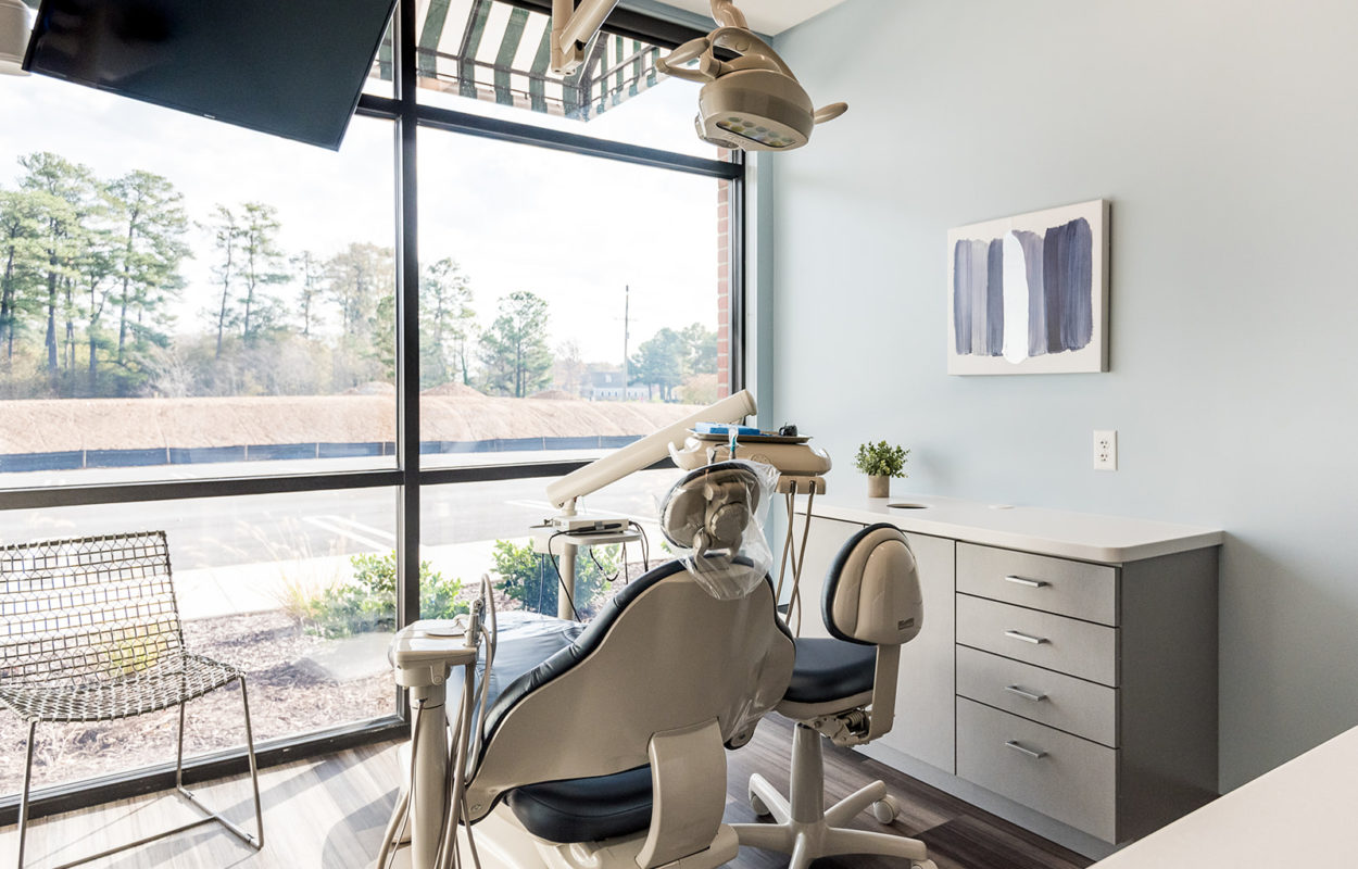 Bright dental operatory featuring a treatment chair, workstation, and floor-to-ceiling windows overlooking the exterior
